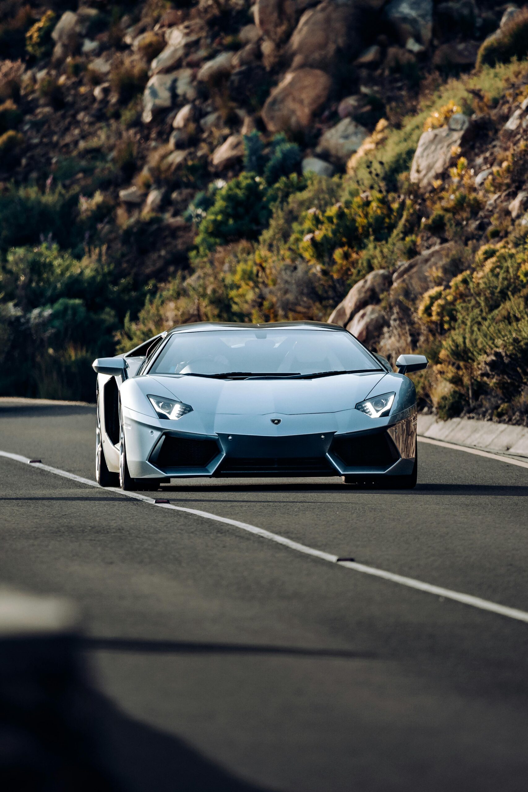 A stunning Lamborghini Aventador driving on a scenic road with rocky hillsides.